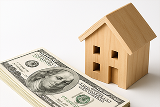 Stack of money next to a miniature house model, representing the financial commitment and funding for stable church planting.